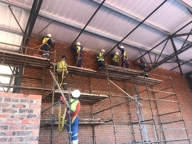 Bricklaying team working from scaffolding in harnesses beneath a steel roof