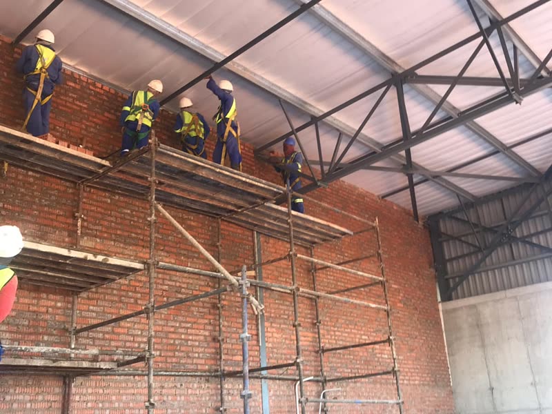 Bricklayers in harnesses on scaffolding against a face-brick wall
