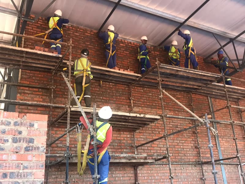 Site team laying brickwork from a scaffold platform inside the building envelope