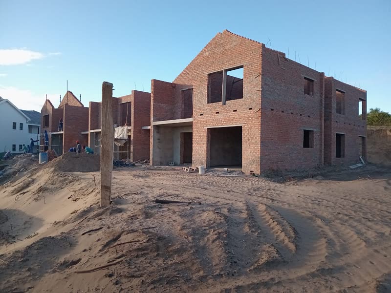Face-brick units rising from a sandy platform, first floor under way