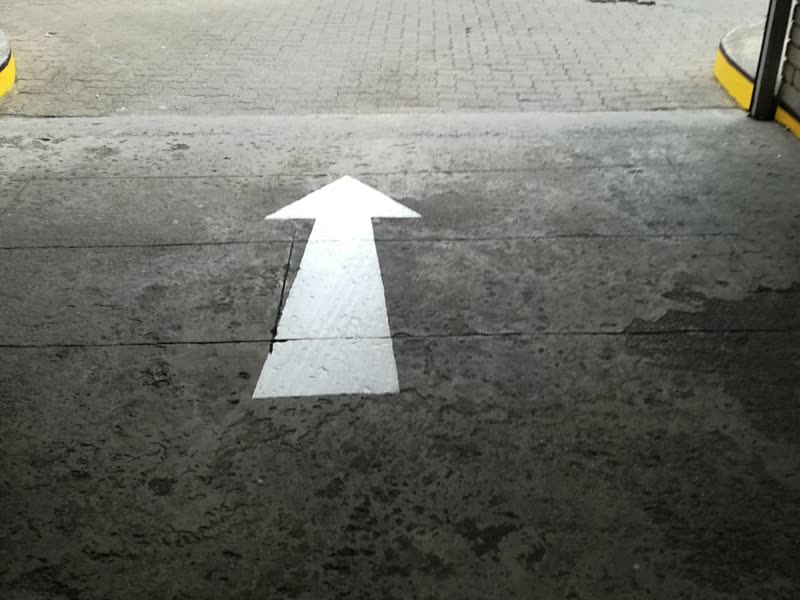 Arrow marking applied to a parking deck floor against a face-brick wall