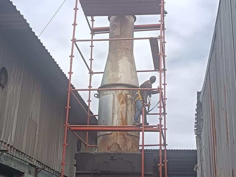 Access scaffold erected around an industrial stack between clad factory buildings