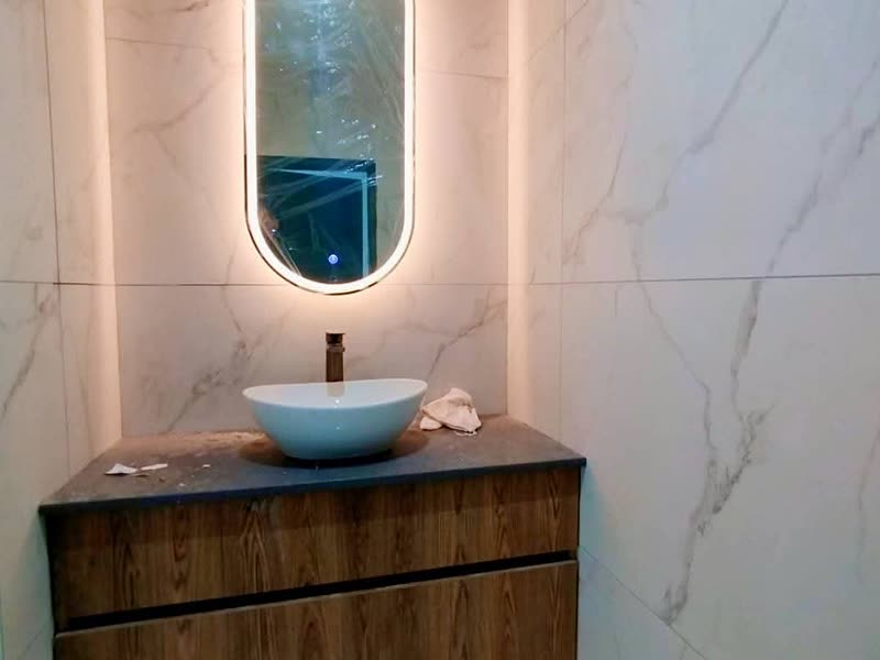 Guest bathroom with a backlit oval mirror and timber vanity on marble-effect tiling