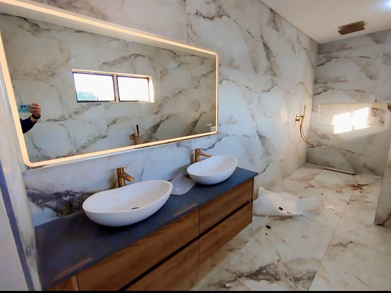En-suite bathroom with twin basins, a brass-framed mirror and marble-effect tiling