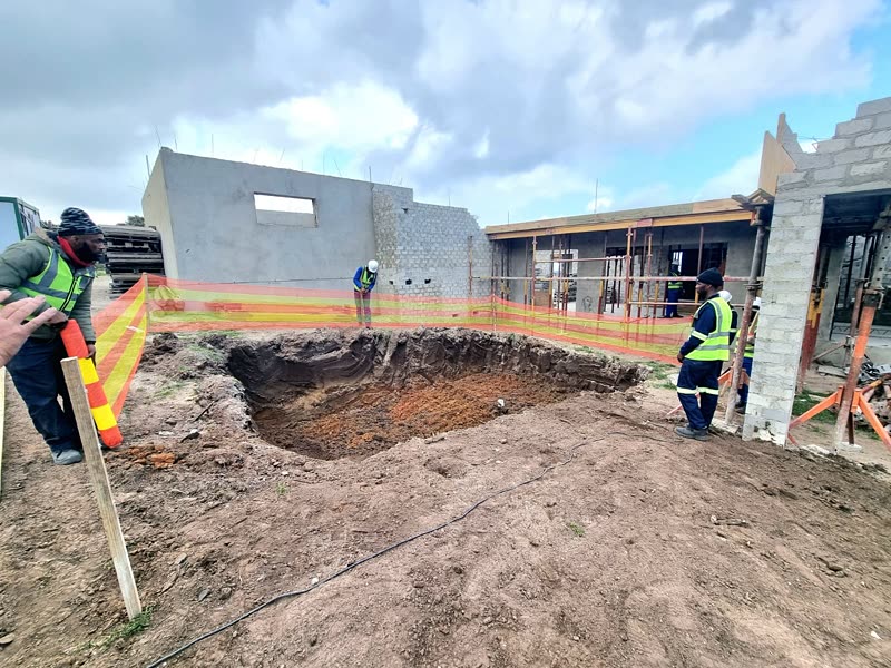 Excavation alongside a partly built house with the site team and barrier tape in place