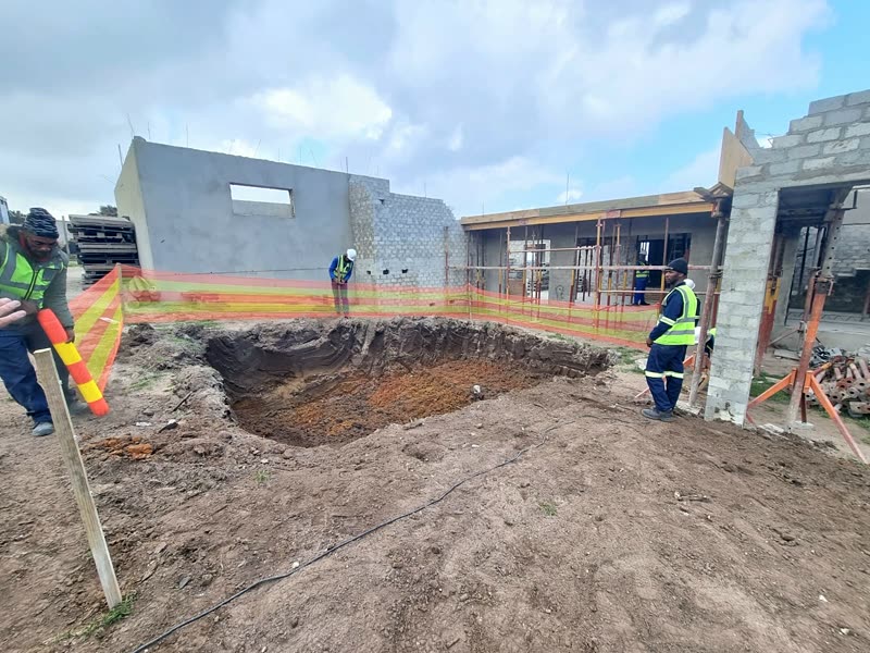 Foundation excavation open beside a rising blockwork superstructure