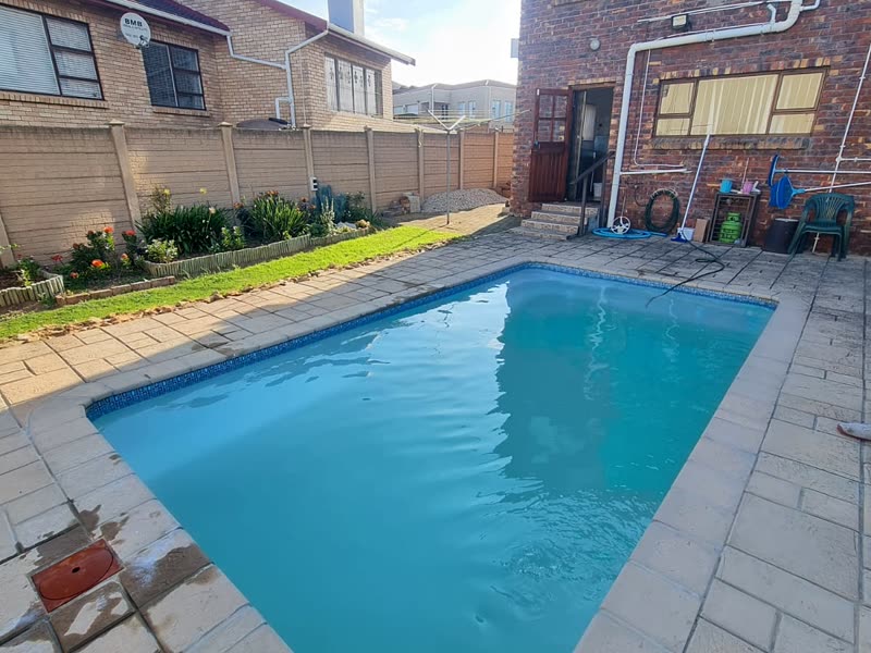 Newly built swimming pool with a paved surround alongside a face-brick home