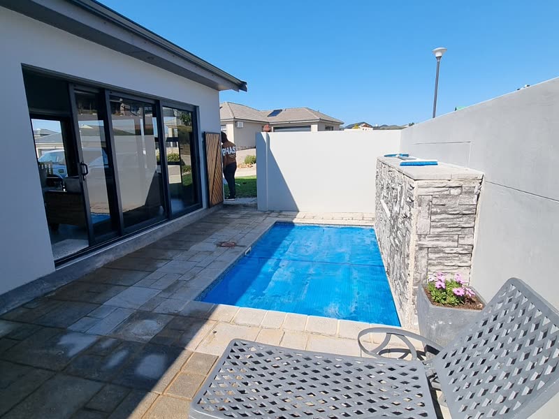 Pool and paved terrace running alongside a modern home with stacking doors